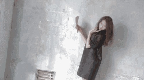 a woman in a black dress is standing in front of a gray wall .