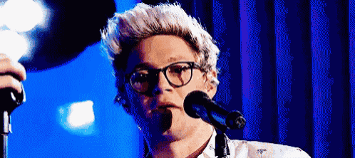 a man is singing into a microphone while wearing glasses .