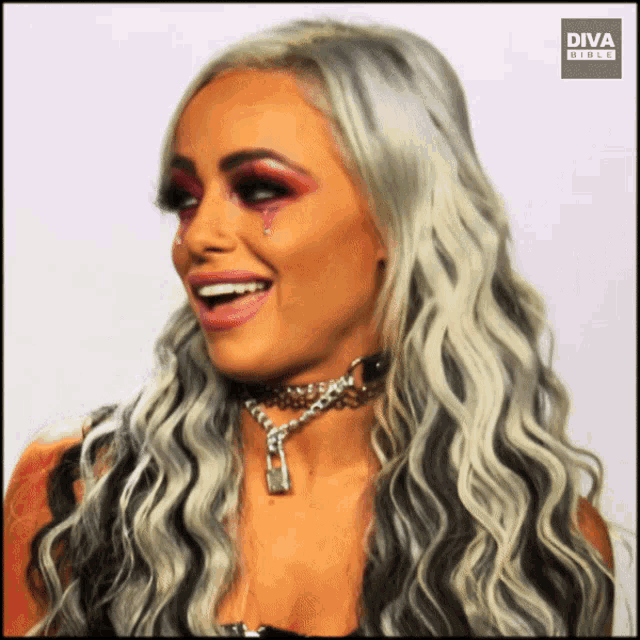 a woman wearing a choker with a padlock on it is smiling with a diva logo in the corner