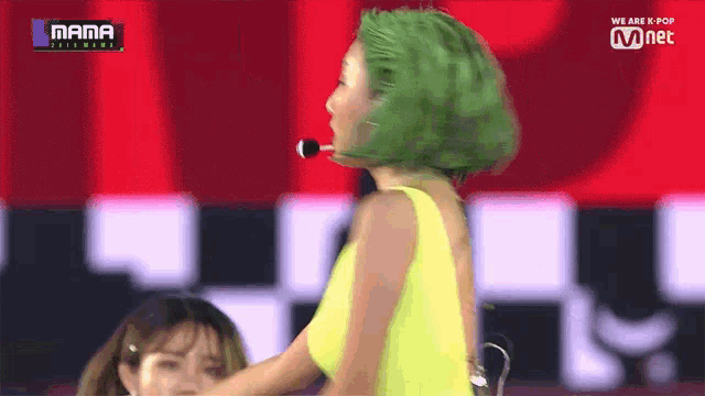 a woman with green hair is on a stage with a mnet logo
