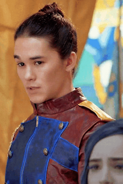 a young man with a bun on his head is wearing a red and blue jacket