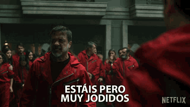 a man in a red jumpsuit says " estais pero muy jodidos " in front of a crowd
