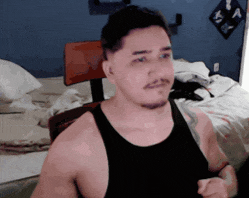 a man in a black tank top is standing in a bedroom