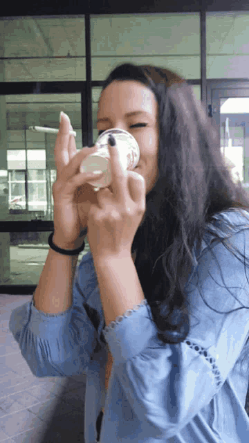 a woman in a blue shirt is holding a cup in her hand