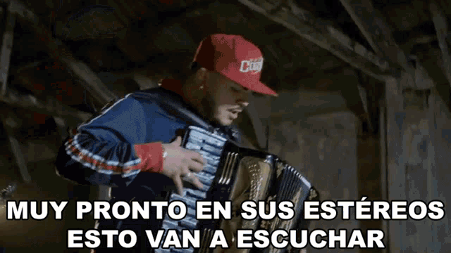a man in a red hat is playing an accordion with the words muy pronto en sus estereos esto van a escuchar below him