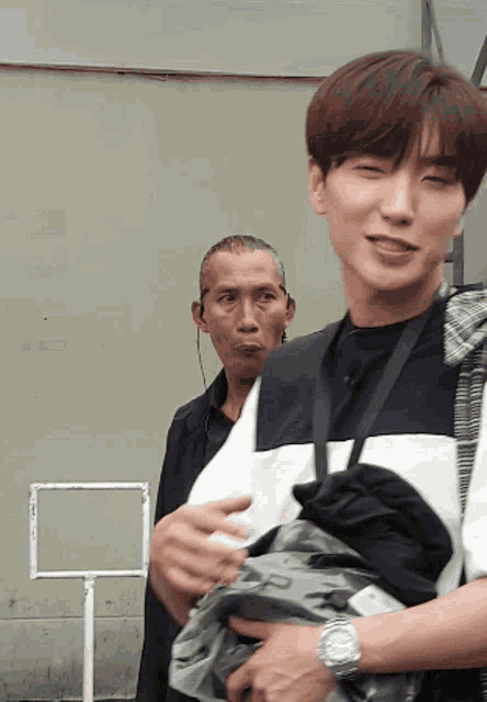 a man wearing a watch stands next to a man wearing earphones
