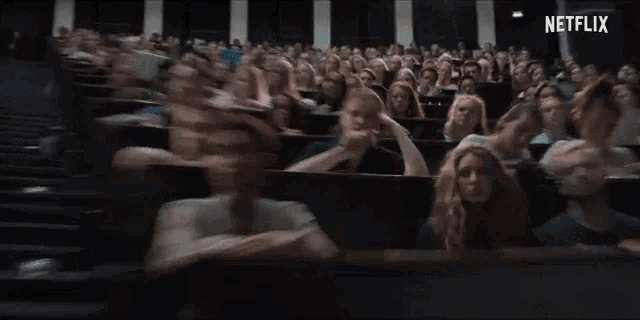 a woman is sitting in a lecture hall with her hand on her face .