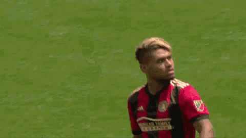 a soccer player wearing a red and black jersey is standing on the field .