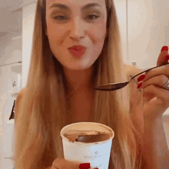 a woman with red nails is eating from a cup that says italia