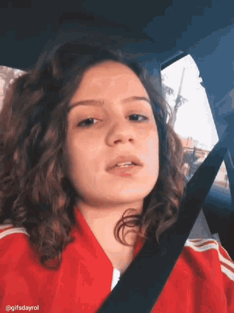 a woman wearing a red jacket is sitting in a car with a seat belt around her neck