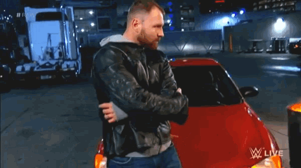 a man in a leather jacket is hugging a red car in front of a fire barrel that says wwe live