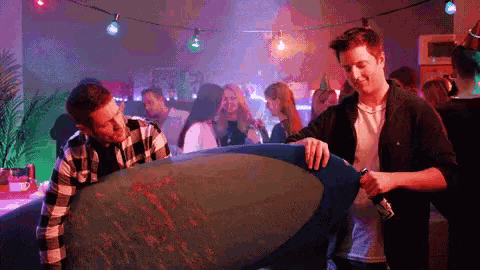 two men are holding a surfboard in a crowded room