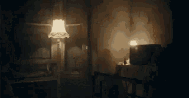 a lamp is lit in a dark room with a bed .