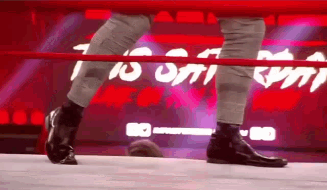 a wrestler is standing in a wrestling ring with his feet taped to the ropes .