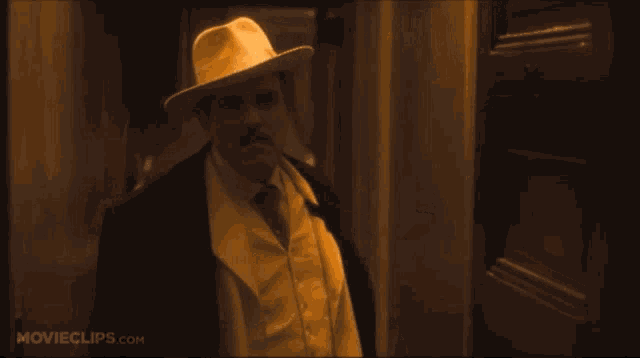 a man in a suit and hat stands in front of a door with movieclips.com written on the bottom