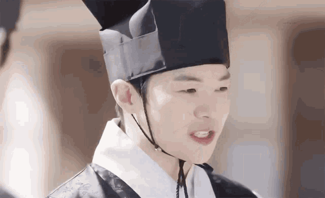 a man wearing a black hat and a traditional korean dress is making a funny face .