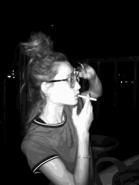 a woman wearing glasses is smoking a cigarette in the dark