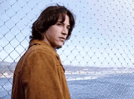 a man standing behind a chain link fence looking out over the ocean