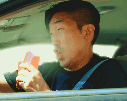 a man wearing a black shirt with the word tommy on it is driving a car