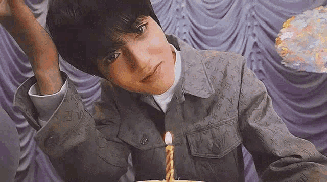 a young man in a louis vuitton jacket is sitting in front of a birthday cake with a candle .