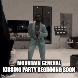 a man in a suit is dancing in a living room with the words `` mountain general kissing party beginning soon '' .