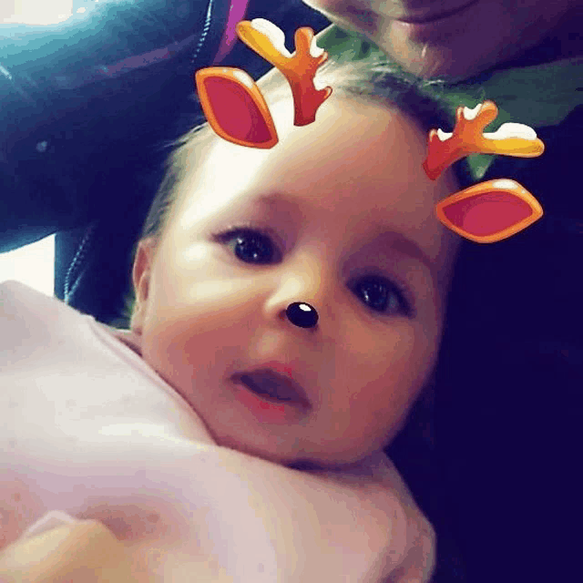 a baby with reindeer antlers on her head is being held by a woman