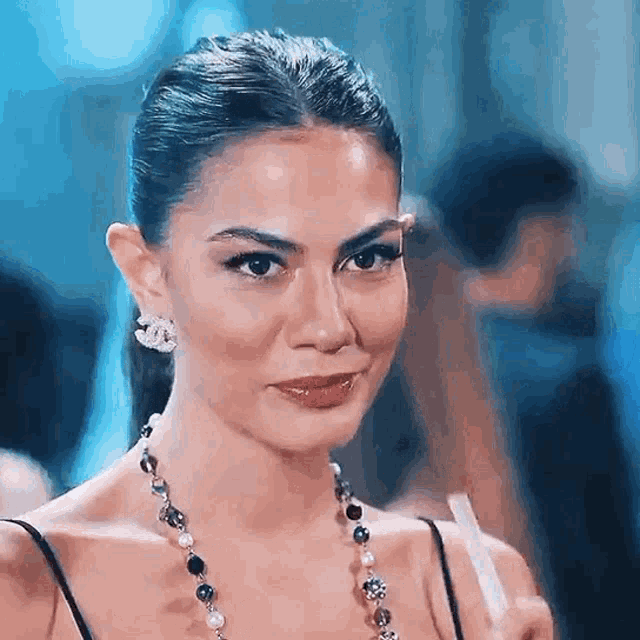 a woman wearing a necklace and earrings looks at the camera .