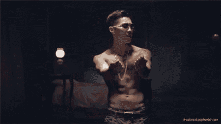 a shirtless man is standing in a dark room with his arms outstretched .
