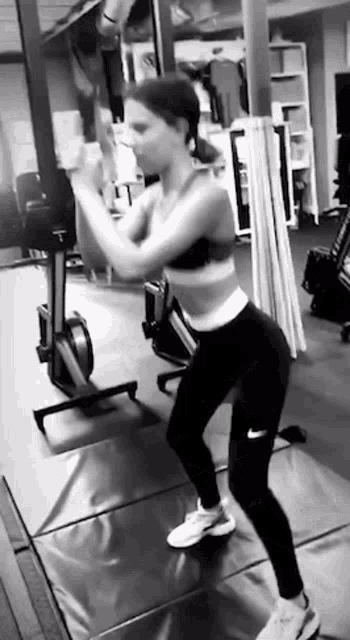 a woman is doing squats in a gym while wearing a sports bra and leggings .