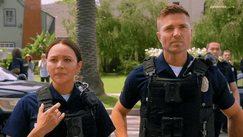 a man and a woman in police uniforms are standing next to each other in front of a palm tree
