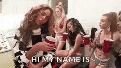 a group of women are sitting around a table holding red cups and drinking .