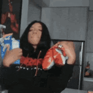 a woman in a black hoodie is holding a bag of chips in her hand