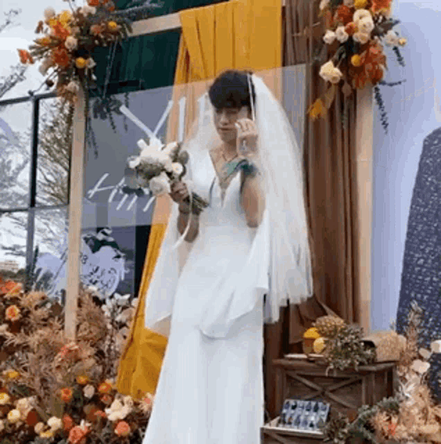 a bride in a wedding dress is holding a bouquet of flowers and talking on a cell phone .