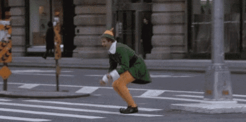 a man in a green elf costume is squatting down on the street .