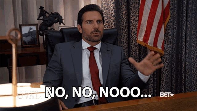 a man in a suit and tie is sitting at a desk and saying no no nooo