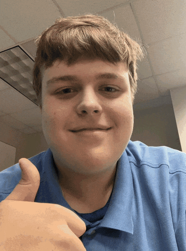 a young man in a blue shirt gives a thumbs up sign