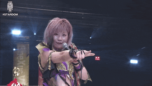 a woman with pink hair is holding a microphone in front of a banner that says #stardom