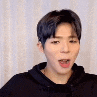 a young man wearing a black hoodie is making a funny face with his mouth open .