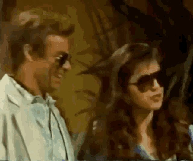a man and a woman are standing next to each other and the woman is wearing sunglasses