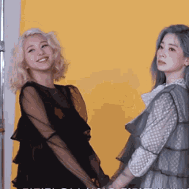 two women are standing next to each other on a yellow background .