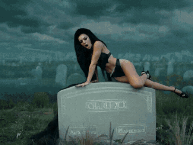 a woman in black lingerie is kneeling on a gravestone that says charli xcx