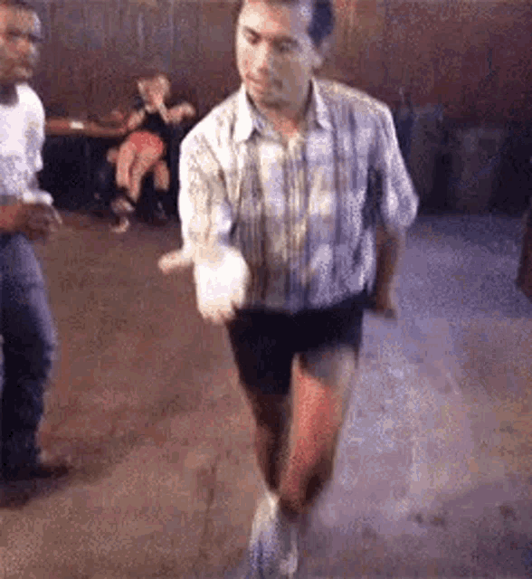 a man in a plaid shirt and shorts is dancing in a room with other people .
