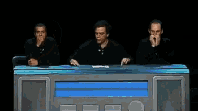 three men are sitting at a table with their hands on their mouths