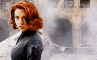 a woman with red hair is standing in front of a building looking at the camera .