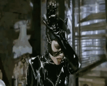 a woman in a catwoman costume is standing in front of a window covering her face with her hand .