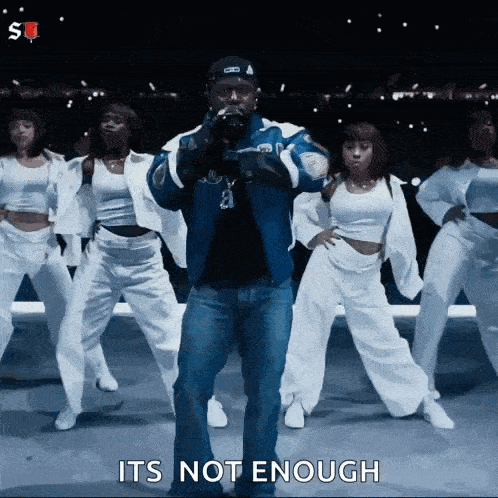 a man is standing in front of a group of dancers and says it 's not enough .