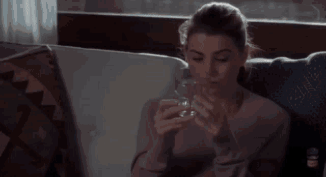 a woman sitting on a couch drinking from a glass