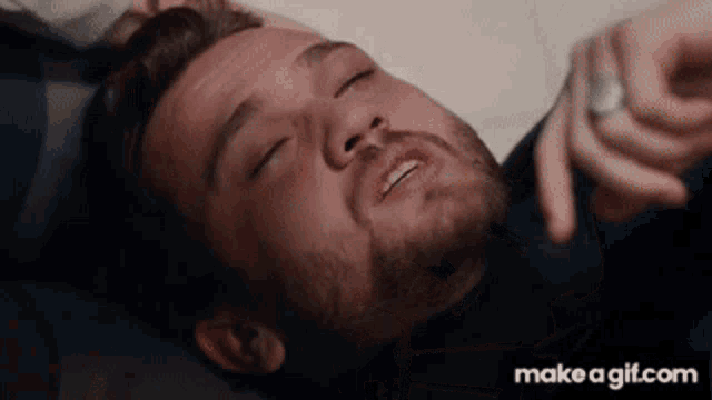 a man with a beard is laying on the floor with his eyes closed and a ring on his finger .