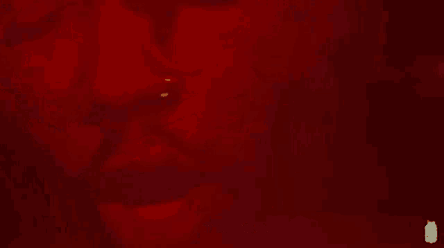 a close up of a person 's face in a dark room with a red background