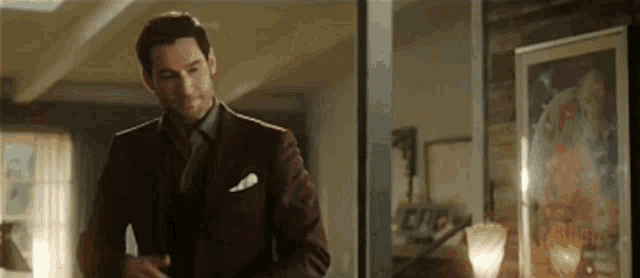 a man in a suit and tie is standing in a living room with a picture on the wall .